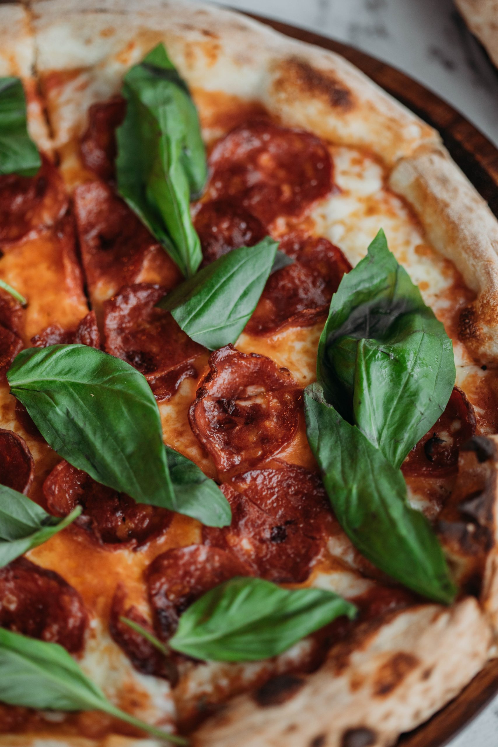 A pizza topped with pepperoni and basil leaves.